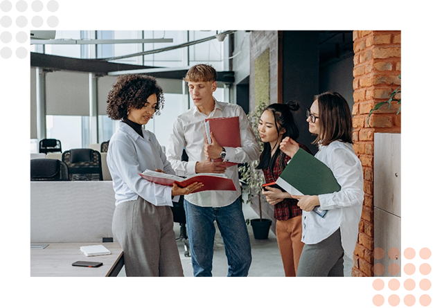Four professionals discussing and holding documents in a modern office setting.