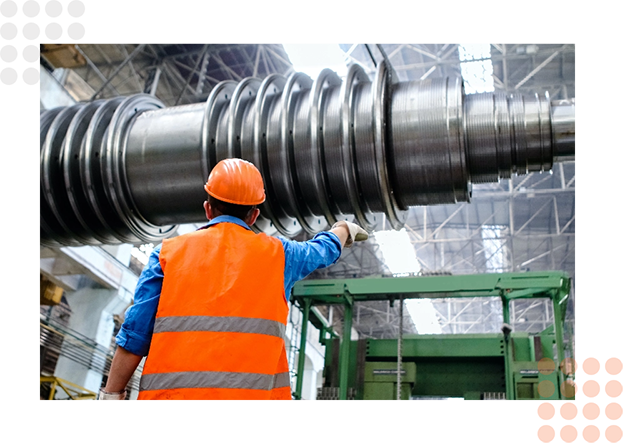 A worker in safety gear oversees large machinery in a manufacturing facility.