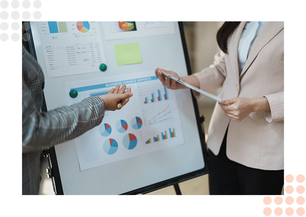 Two professionals discuss data on a presentation board with charts and graphs.