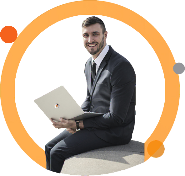 Smiling man in a suit holding a laptop while sitting on a chair.