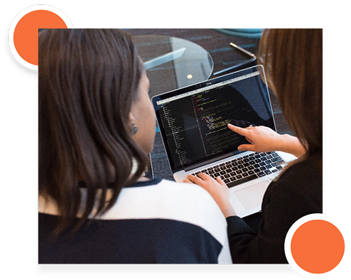A woman pointing at a laptop screen displaying code and data migration tasks.