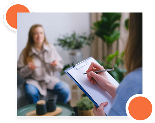 Two women discussing project details, one taking notes on a clipboard during a meeting.