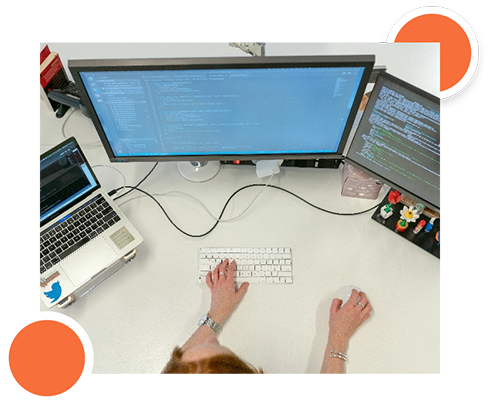 Hands typing on a keyboard, working on custom code at a desk with multiple monitors