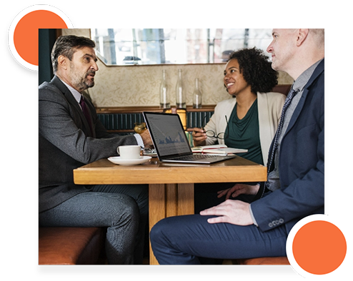 Two professionals discussing project plans at a table with a laptop and documents.
