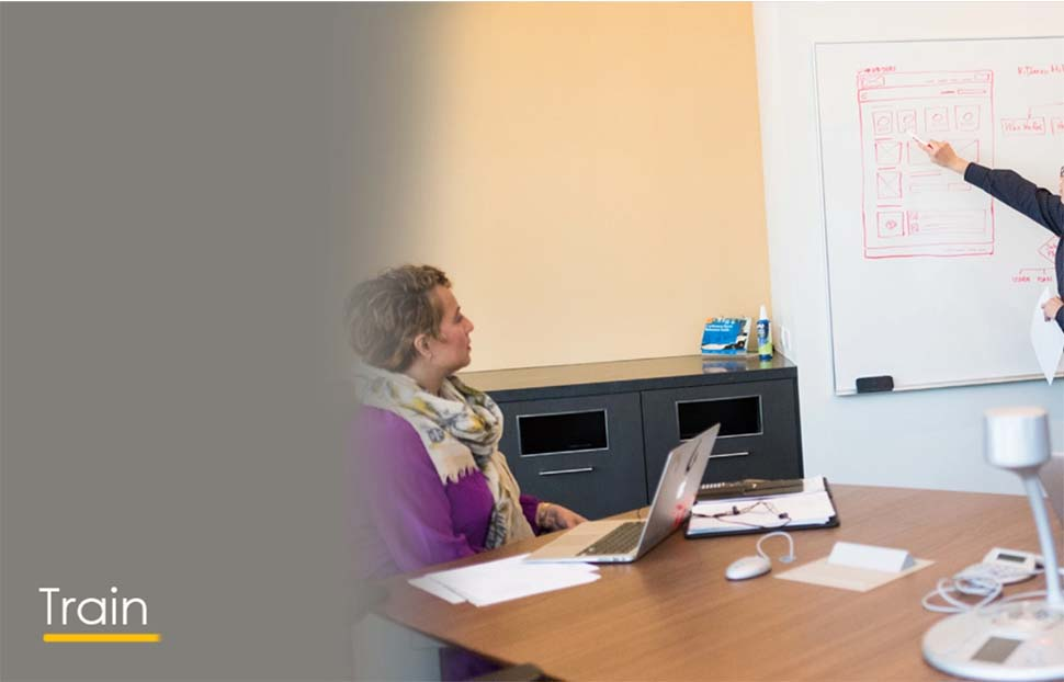 A woman presenting to a group in a training session with a whiteboard.