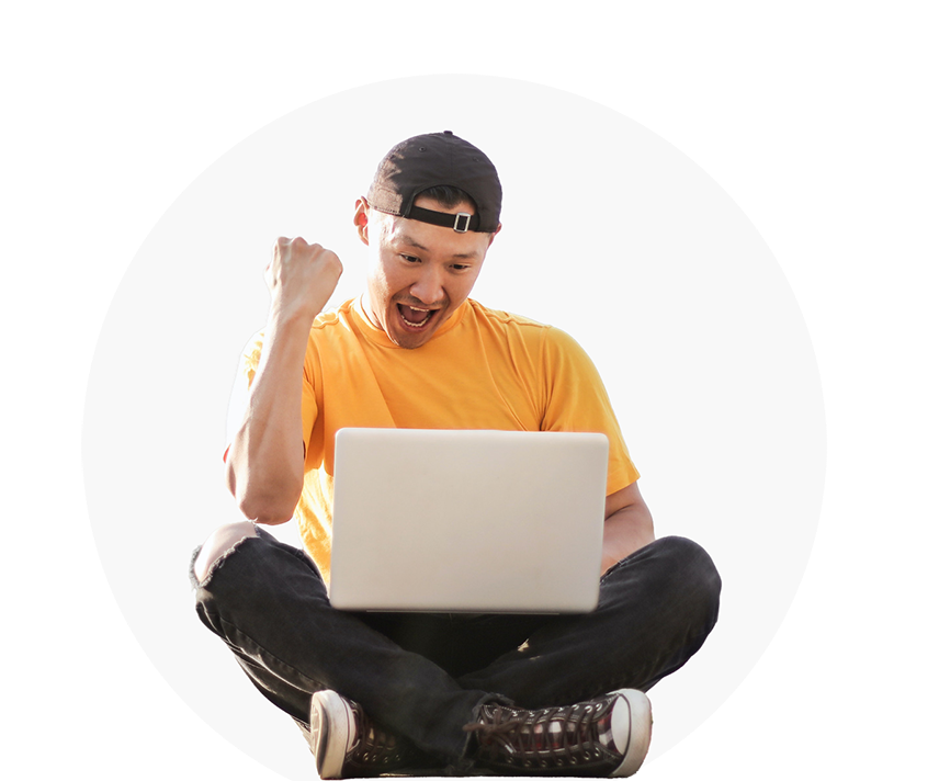 A happy man in a yellow shirt celebrating while using a laptop on the floor.