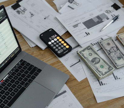 Laptop and smartphone displaying financial data on a desk with scattered paper documents and dollar bills, symbolizing financial management through Dynamics 365 FO.
