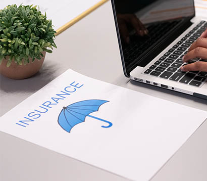 Document labeled 'Insurance' with blue umbrella graphic on desk next to laptop, representing financial and operations management context.