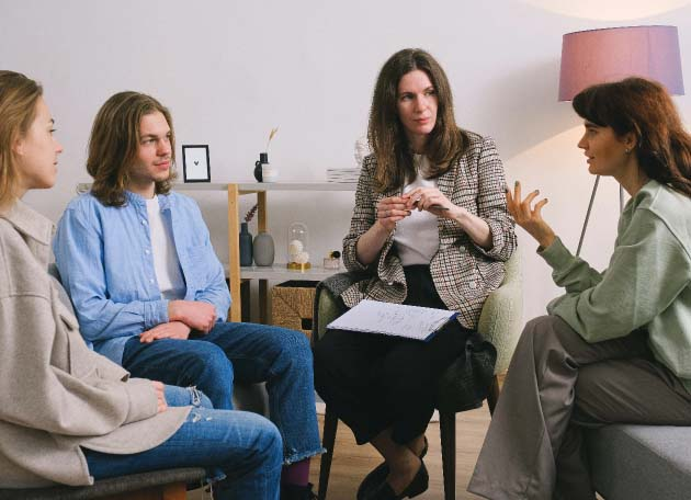 A diverse group of four people engaged in a discussion in a modern office setting, representing collaborative business solutions. The scene includes a woman with a notepad, suggesting a focus on SharePoint strategies and teamwork.